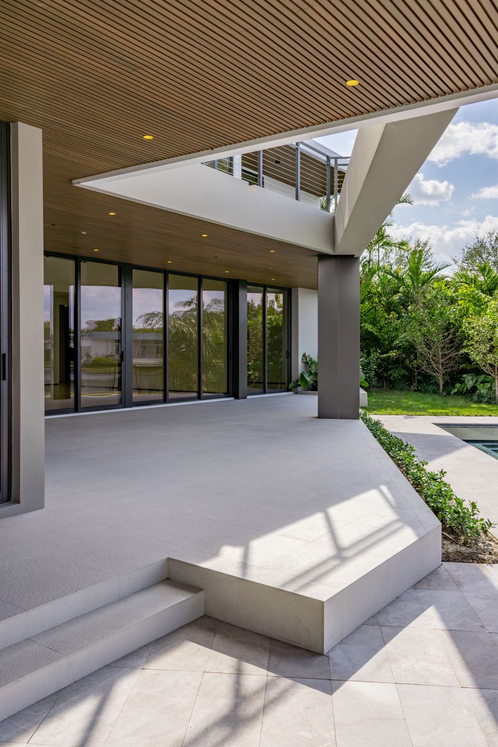 Modern covered patio area with wooden slatted ceiling and minimalist white seating built into the structure.