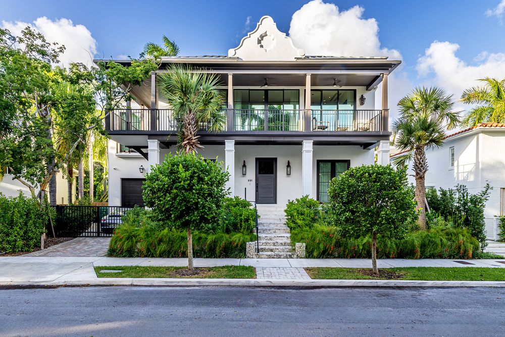 Street view of an elegant modern home with manicured landscaping and paved driveway.
