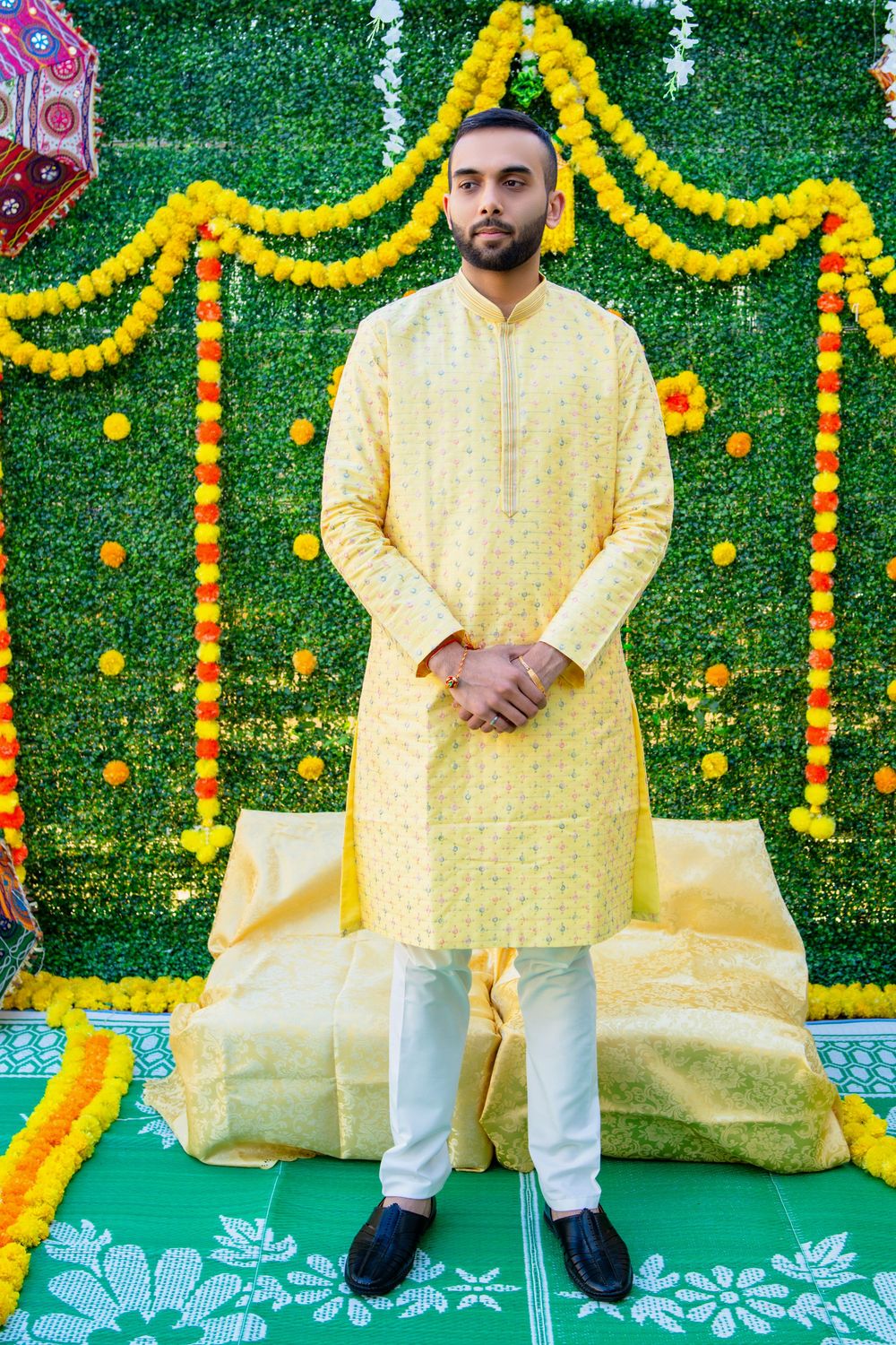 Festive wedding decor with yellow marigold garlands and green backdrop features someone in pale yellow traditional kurta.