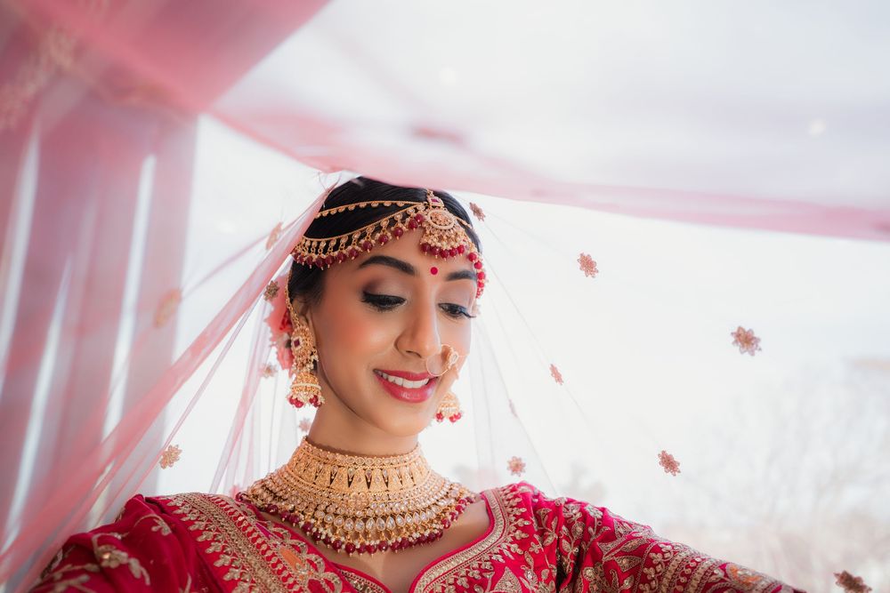 A bride wearing a traditional red and gold Indian wedding lehenga and jewelry poses elegantly during her ceremony.