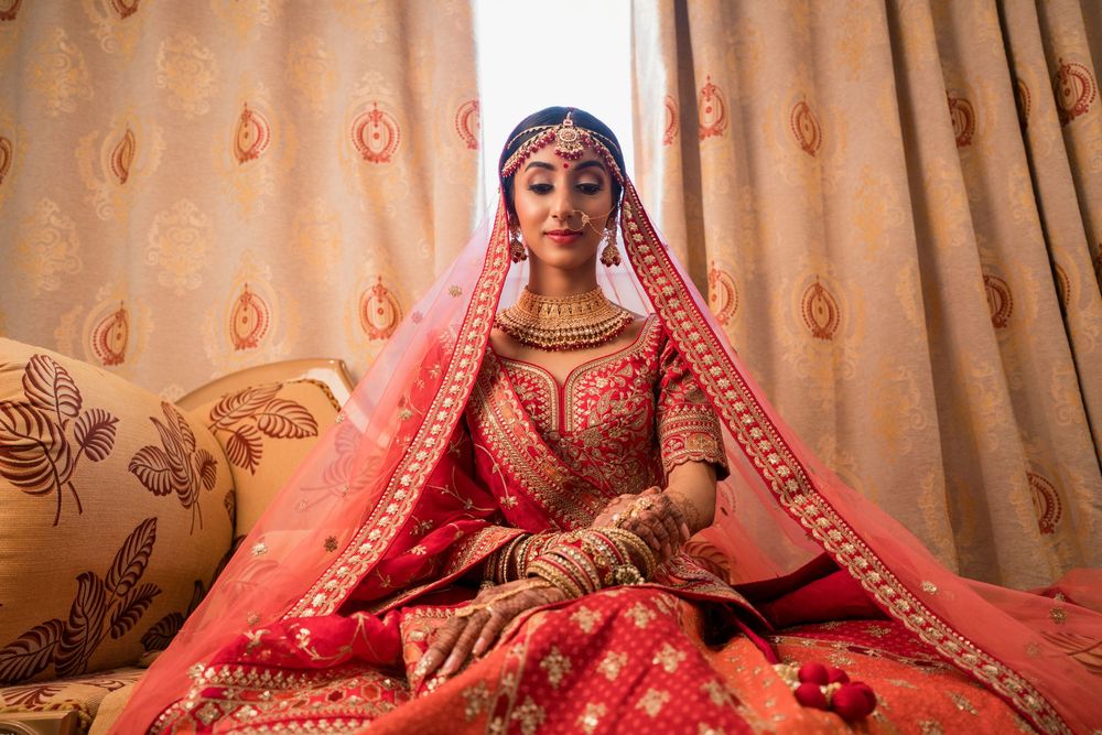 A person in traditional Indian bridal attire with ornate red and gold lehenga sitting in an elegantly decorated setting.