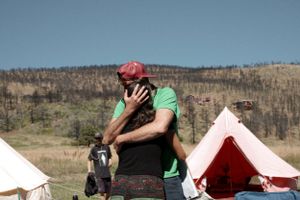 Person in green shirt at a desert campsite with white tents in the background.