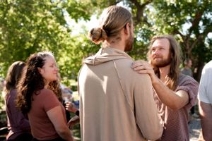 A group of people share warm embraces at an outdoor gathering on a sunny day.