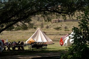 Two large teepee-style tents set up in a grassy field with hills in the background.