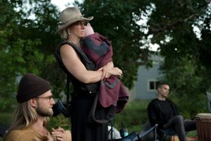 A gathering of people in an outdoor setting with someone wearing a brown hat standing and holding something.