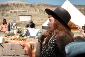 Person wearing a black hat and patterned dress at an outdoor desert gathering with tents.