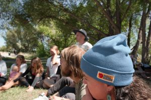 Outdoor gathering with people sitting under trees wearing casual attire.