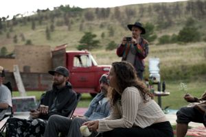 People gathered outdoors with mountains and a red truck visible in the background.