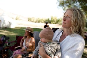 A parent holds a baby while sitting outdoors among others at a casual gathering.