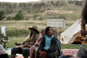 Group of people sitting outdoors on blankets with a teepee visible in the background.