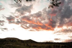 Dramatic sunset sky with pink and orange clouds over mountain landscape silhouette.