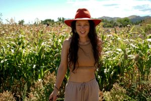 Person in red hat and summer outfit standing in tall cornfield on sunny day.