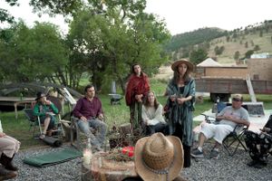 People gathered around a fire pit during an outdoor social event with mountains in the background.