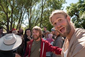 A group of people smile and cheer together outdoors with trees in the background.