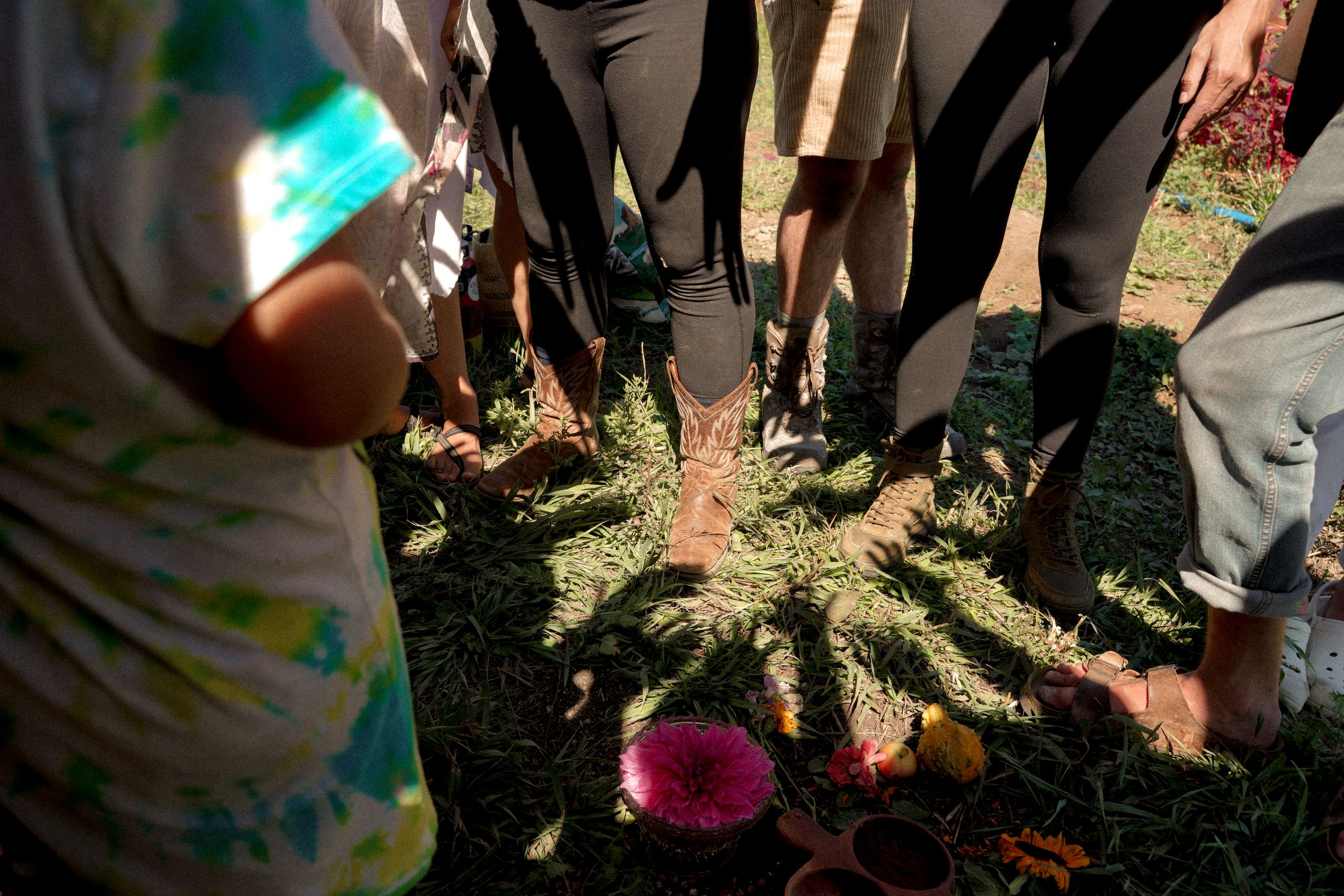 Group standing in circle looking down at harvested vegetables in garden.