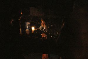 A dim candlelit scene in darkness creates a moody atmospheric environment.