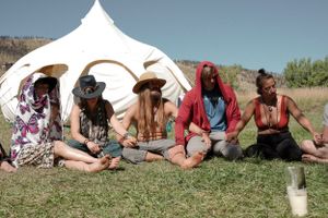 People sitting in front of white tent during outdoor festival.
