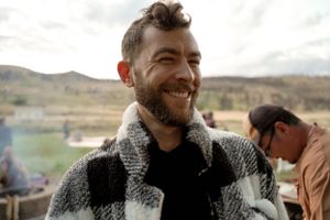 Person in a patterned sweater smiling warmly outdoors against a desert landscape.