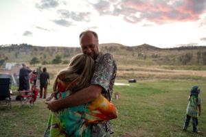 People embracing during sunset in a field with mountains in the background.