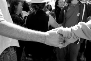 Black and white close-up of two hands clasped together in a crowd.