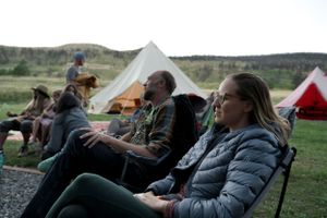 People relaxing in camping chairs at a campsite with tents in a mountainous landscape.