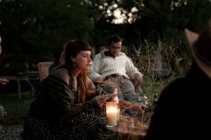 A candlelit outdoor evening gathering with people seated around in conversation.