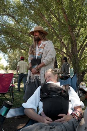 People relaxing outdoors under shady trees at a casual gathering with camping chairs.