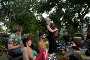 Outdoor gathering with multiple people seated and standing under trees.
