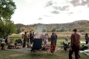 Group of people gathered for outdoor event with camping chairs and mountain backdrop.