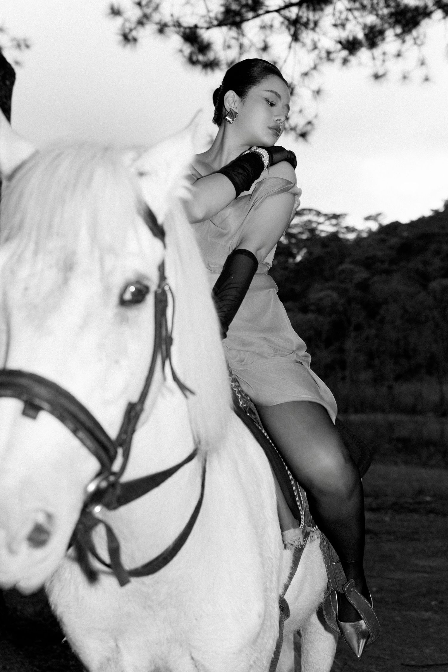 Black and white photo of an elegant woman in a pink dress leaning gracefully on a white horse.