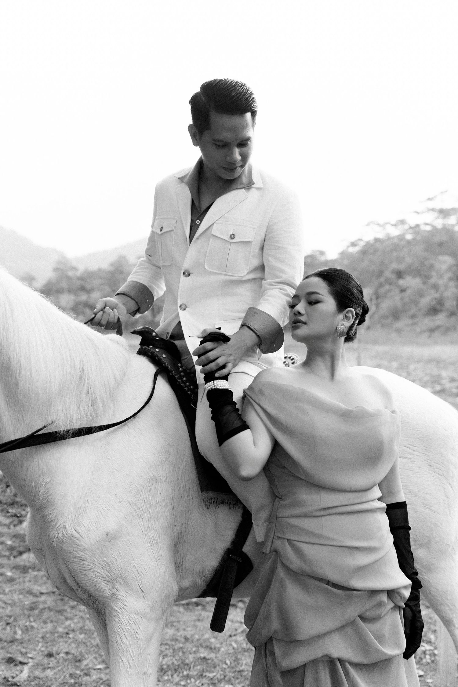 Black and white photo of a man on a white horse reaching down to a woman in an elegant dress.