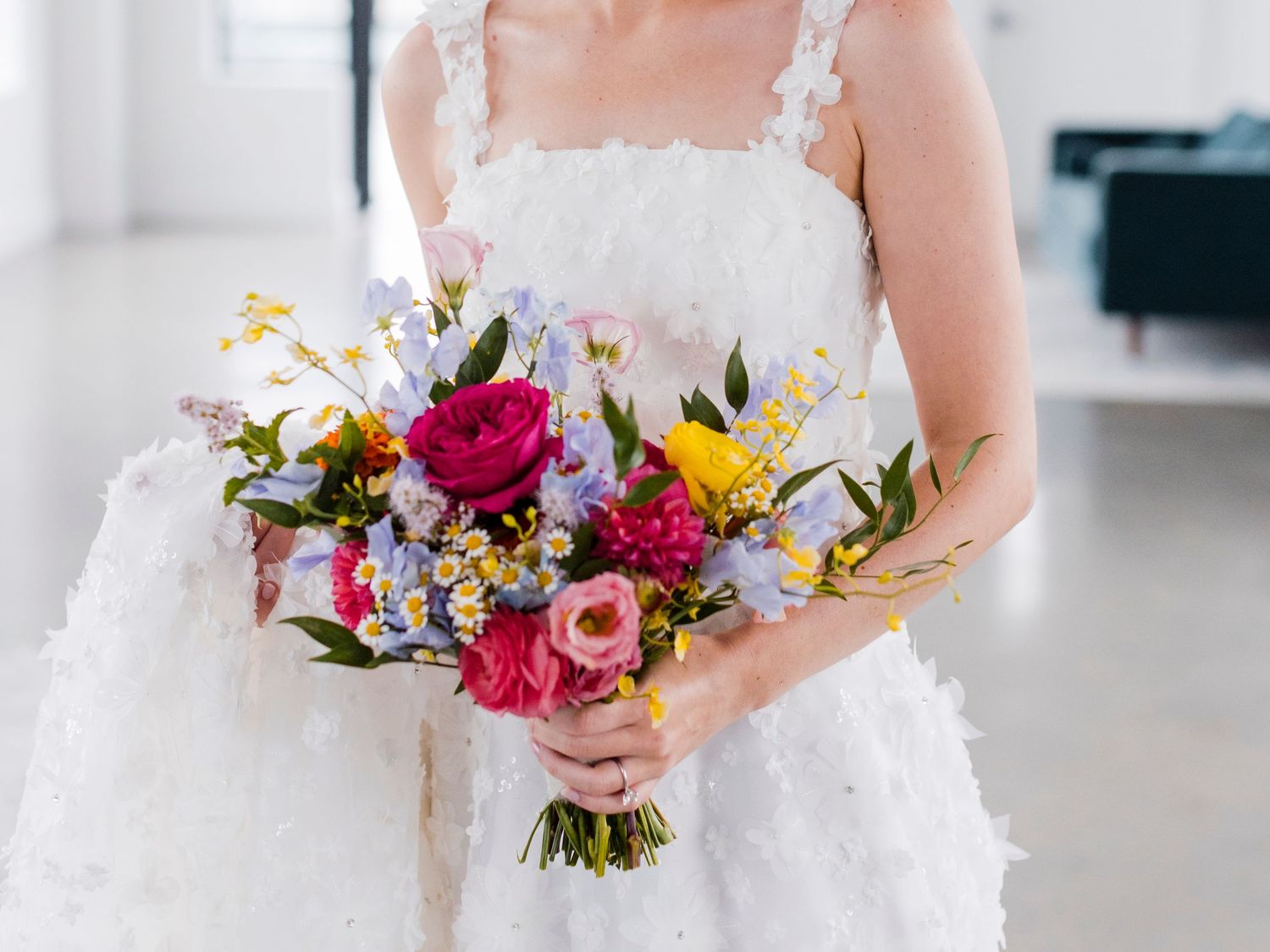 A vibrant bridal bouquet featuring pink roses, yellow flowers, and mixed wildflowers against a white dress.