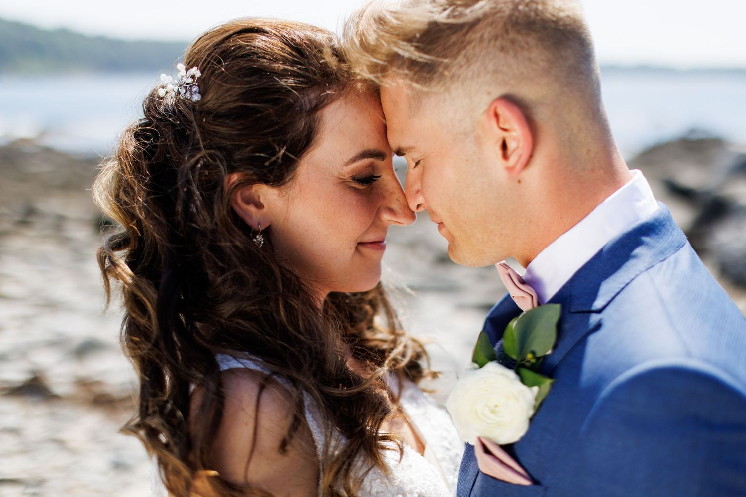 Intimate wedding portrait captured against a blurred coastal background.