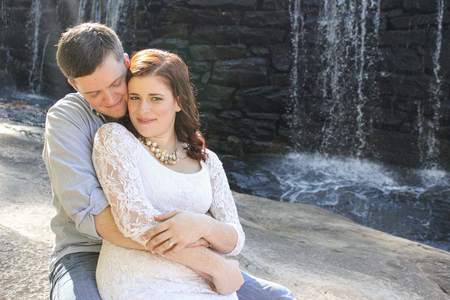 Romantic couple embracing by a cascading waterfall with rocky backdrop.