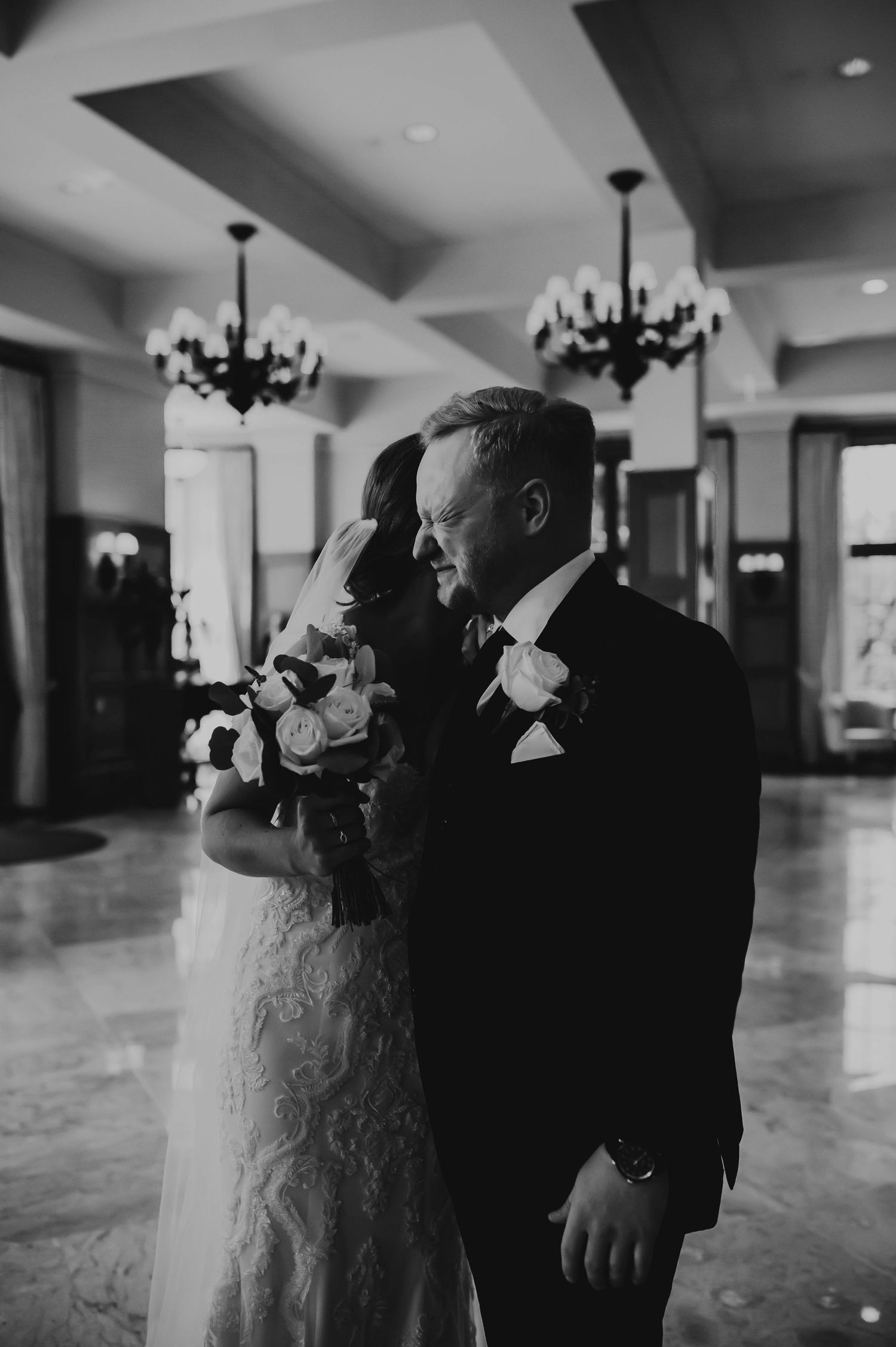 Elegant black and white wedding photo in a grand ballroom with vintage chandeliers and marble floors.