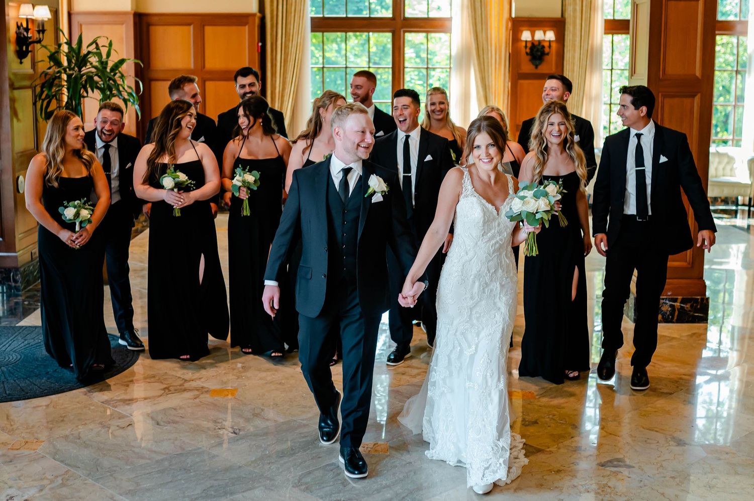 Wedding party in formal attire celebrating in an elegant venue with black dresses and marble floors.