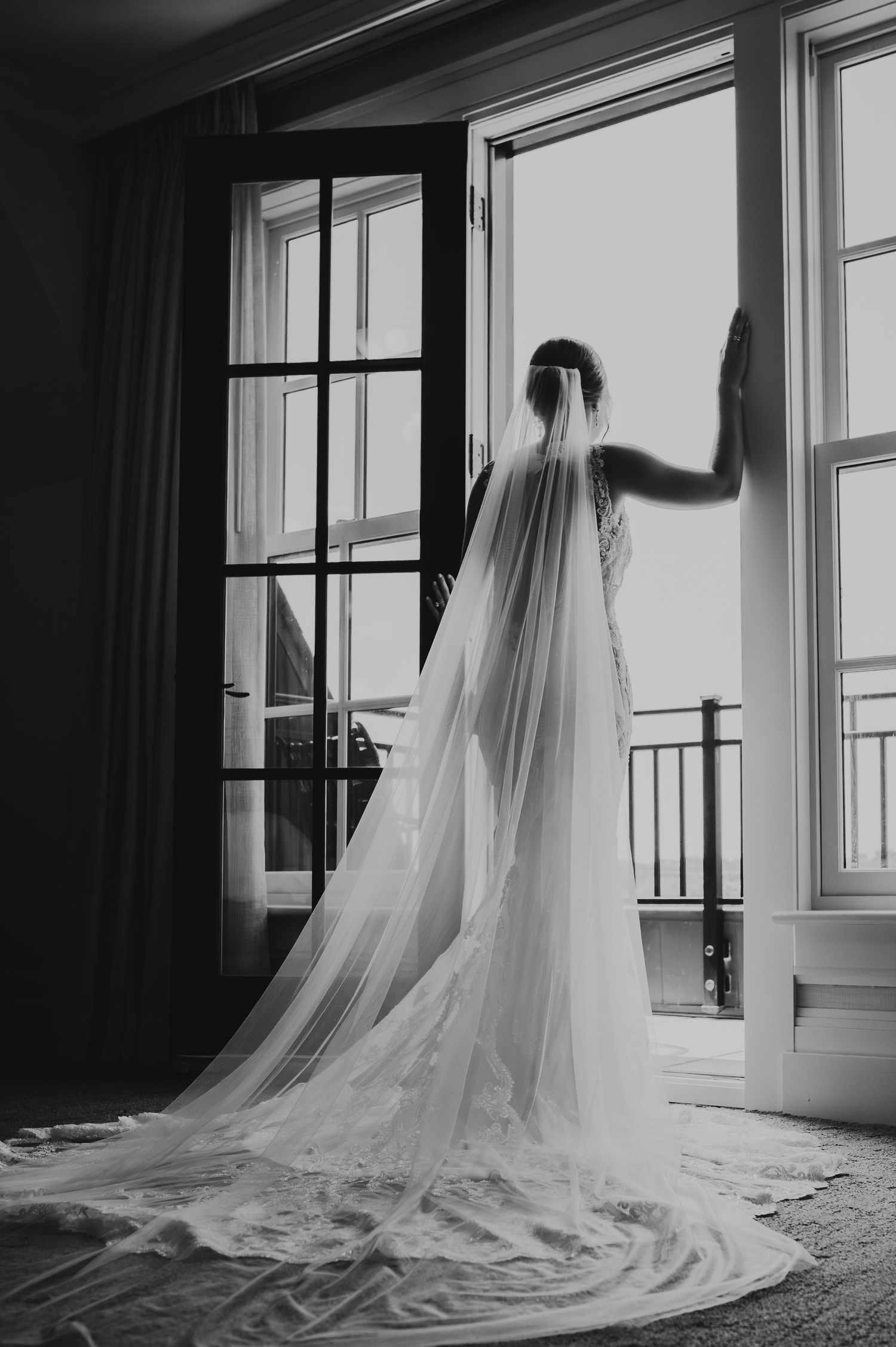 A delicate bridal veil cascades elegantly down a hardwood floor in a naturally lit room, captured in black and white.