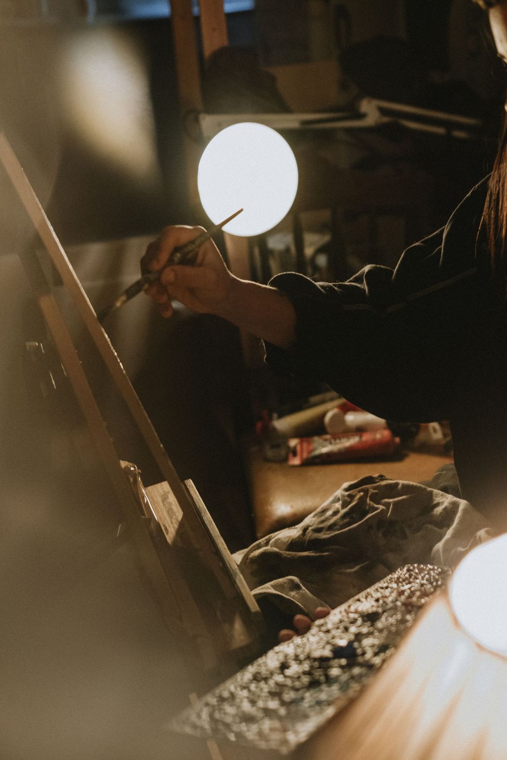 A dimly lit desk with art supplies and papers illuminated by a soft lamp glow.