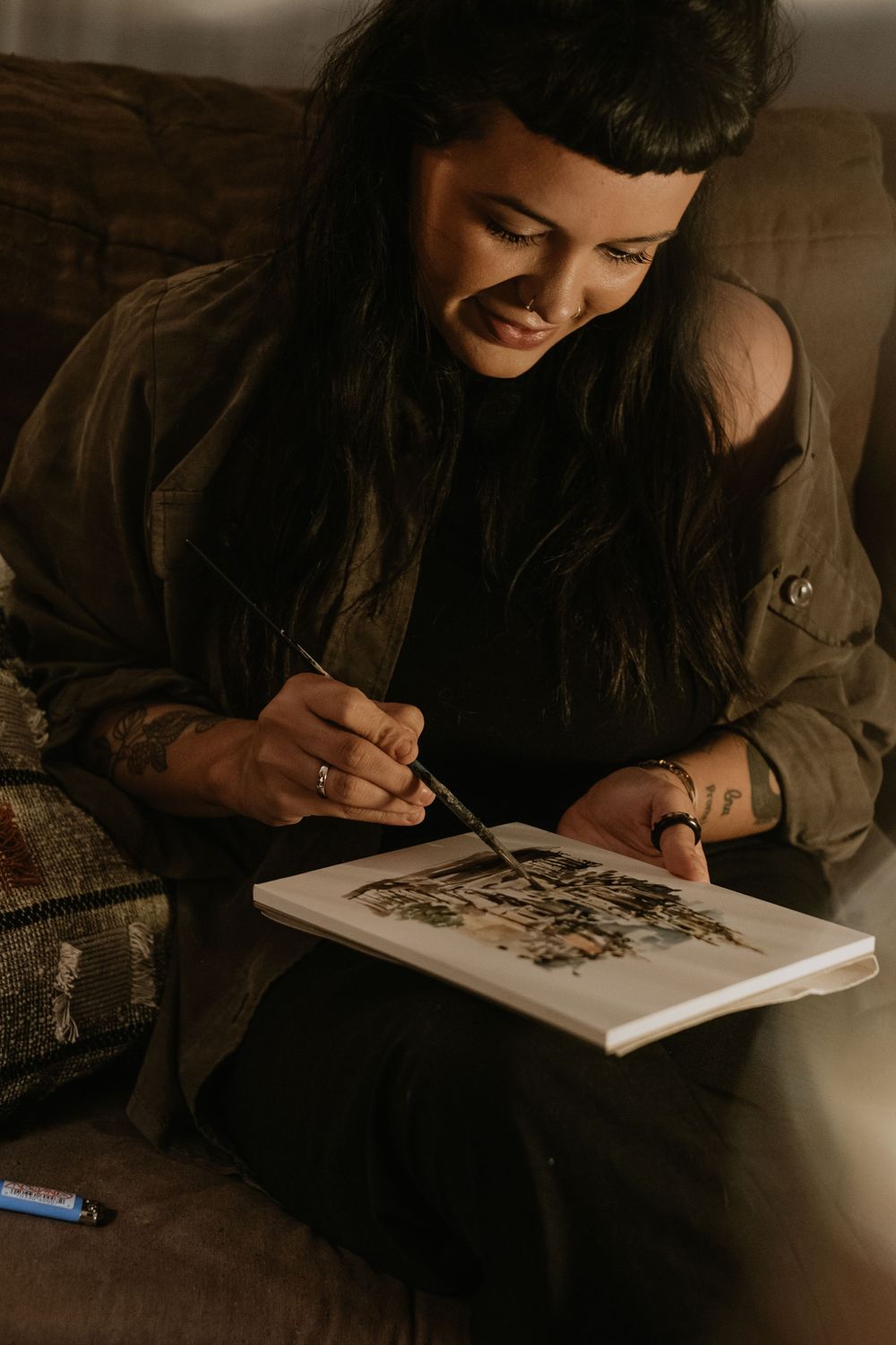 An artist sketching in a notebook under warm lamp light.