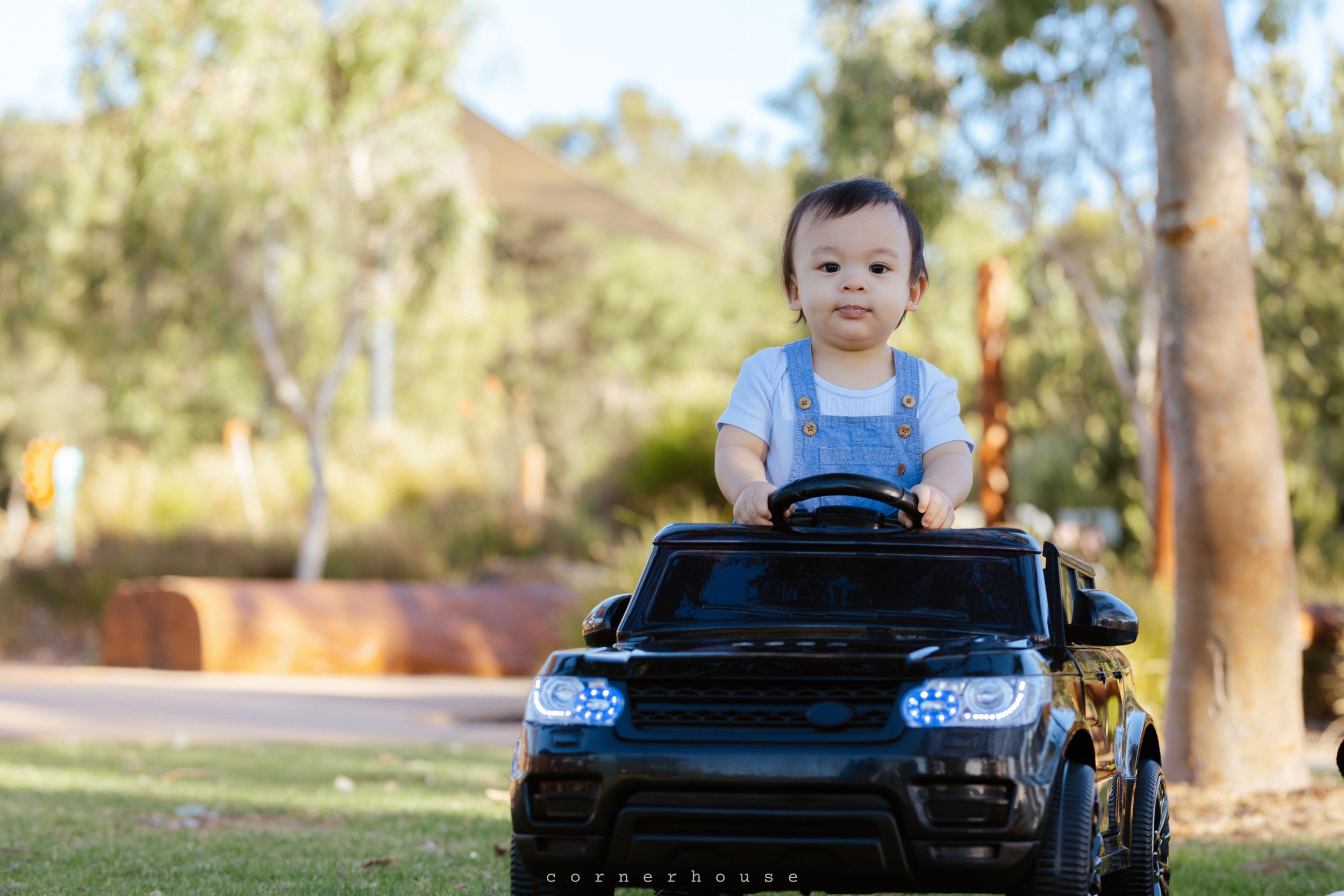 Small child riding in a black toy Range Rover electric car outdoors on a sunny day.