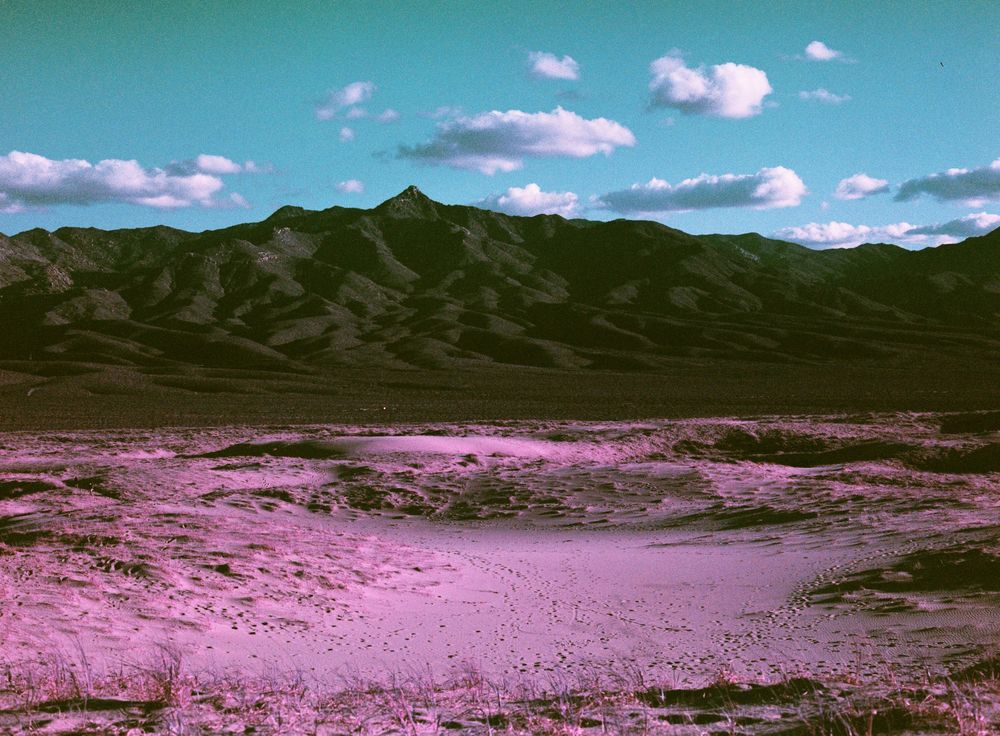 Mountain landscape with pink-tinted desert terrain under bright blue sky.