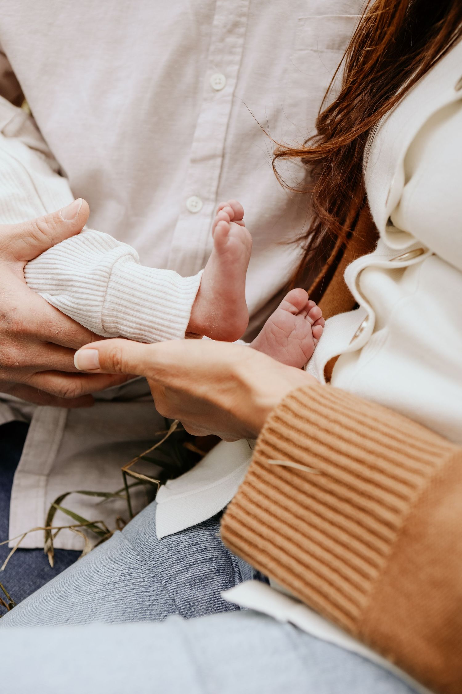 Close-up view of tiny baby feet being gently held by hands in white sleeves against soft textured fabrics.