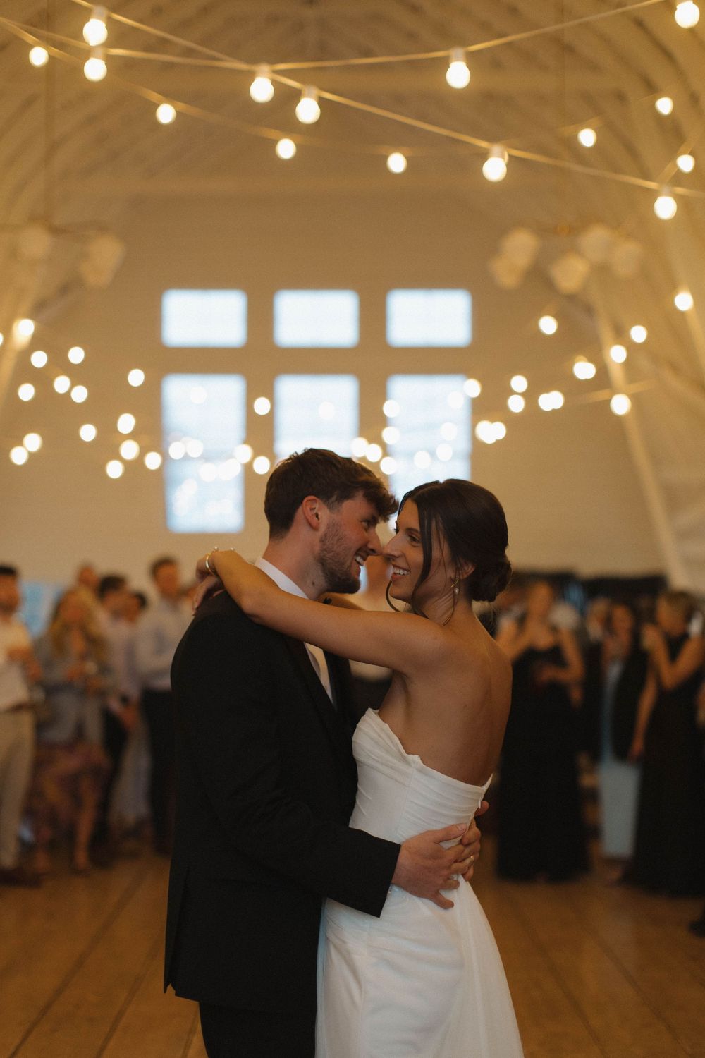 A couple shares an intimate dance moment under warm string lights at a wedding reception.