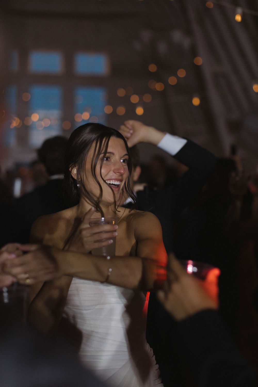 A bride in white laughs joyfully while dancing at her wedding reception.