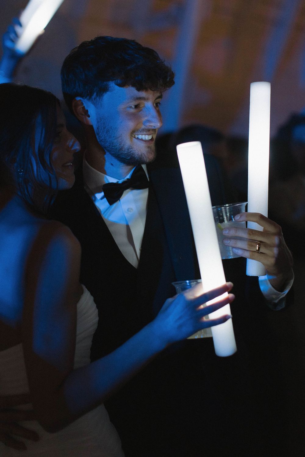 Wedding guests holding glowing LED foam sticks during a nighttime celebration.
