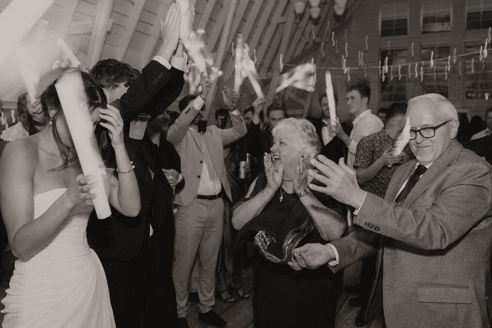 Black and white photo of wedding guests dancing with light-up foam sticks on the dance floor.