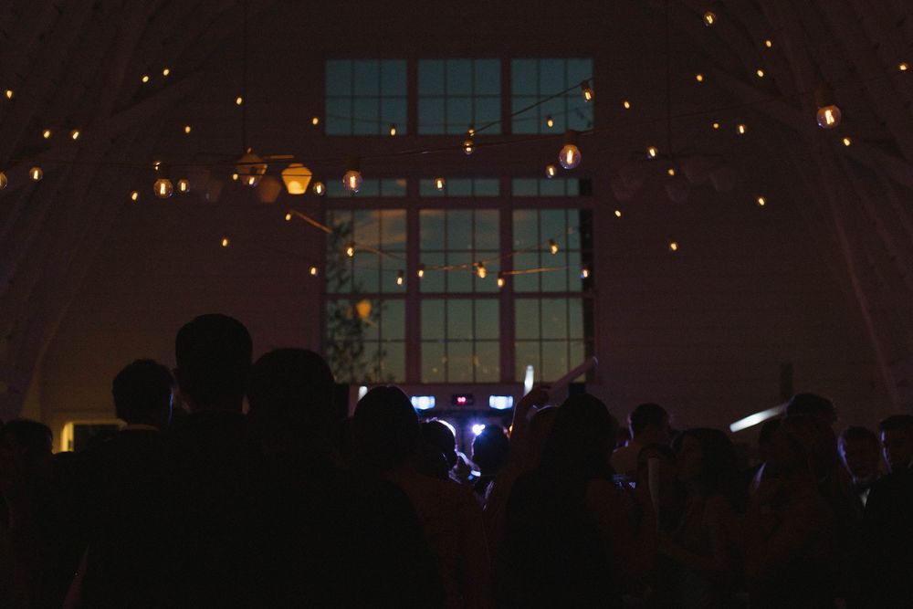 Dark reception venue with silhouettes of guests and twinkling lights in the background.