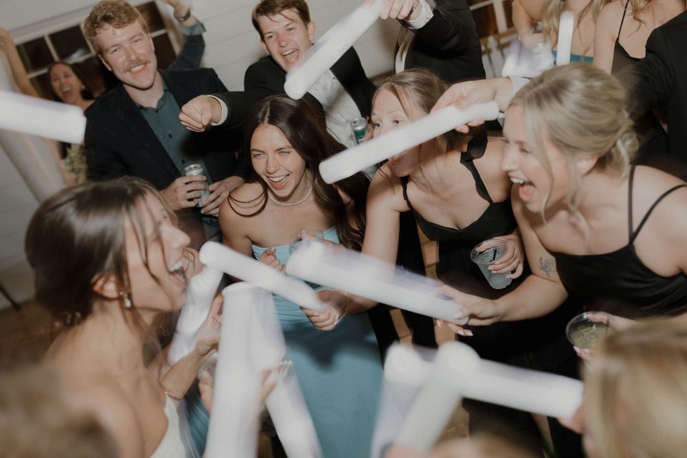 Wedding party members holding illuminated foam sticks during a reception celebration.