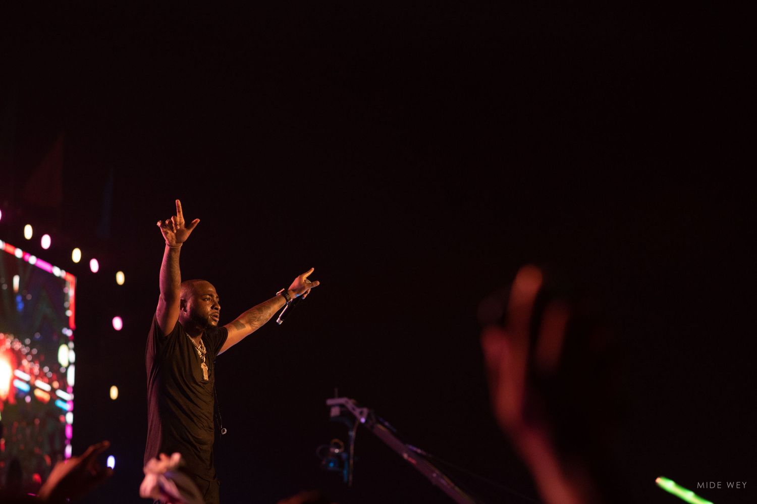 Silhouetted concert performers on stage with dramatic lighting and raised hands create an energetic atmosphere.