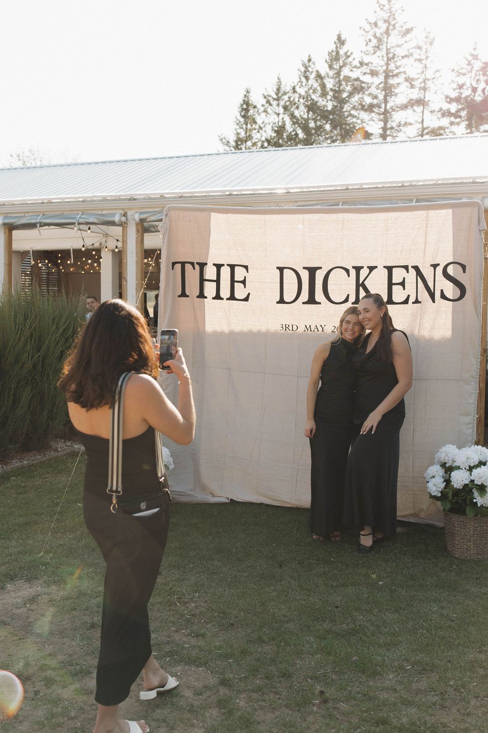 Group of people gathered outdoors near a white wall with 'The Dickens' signage.